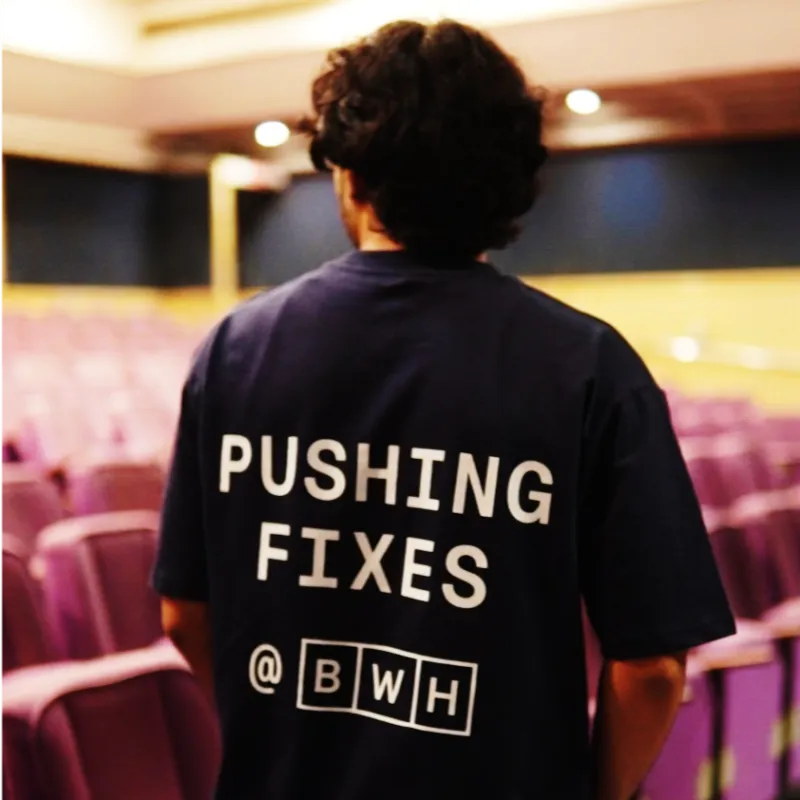 Kaushal Shriwas from behind in an empty auditorium, wearing a tee that reads Pushing fixes @ BWH